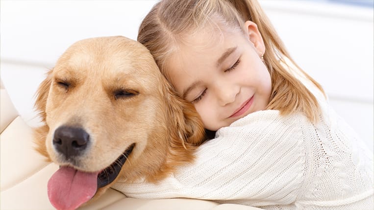 A young girl gently hugging a Golden Retriever, showing love and affection